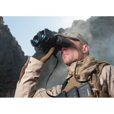 Osoba s binokulárom Armasight DARK STRIDER Gen 1+ používa nočné videnie v teréne, v pozadí vidieť hornatú krajinu. Osoba má na sebe outdoorové oblečenie a šatku.