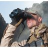 Osoba s binokulárom Armasight DARK STRIDER Gen 1+ používa nočné videnie v teréne, v pozadí vidieť hornatú krajinu. Osoba má na sebe outdoorové oblečenie a šatku.