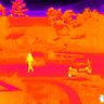 Termovízny pohľad z kamery FLIR Scout TK, zobrazený obraz s farebnou paletou InstAlert, na ktorom sú vidieť osoby a vozidlá v teréne.