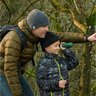 Otec so synom pozorujú prírodu pomocou termovízie FLIR Scout TK v lese. Obaja sú oblečení v zimných bundách a čiapkach. Syn drží termovíziu a pozerá cez ňu, zatiaľ čo otec ukazuje smer pozorovania.